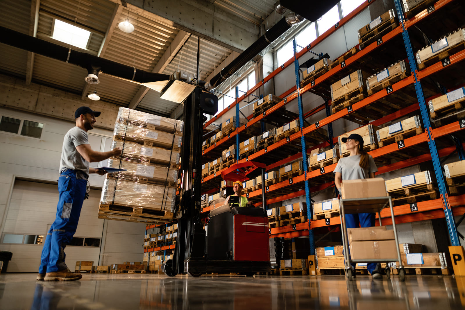 Warehouse staff guiding a reach truck lifting a wrapped pallet beside rows of pallet racking